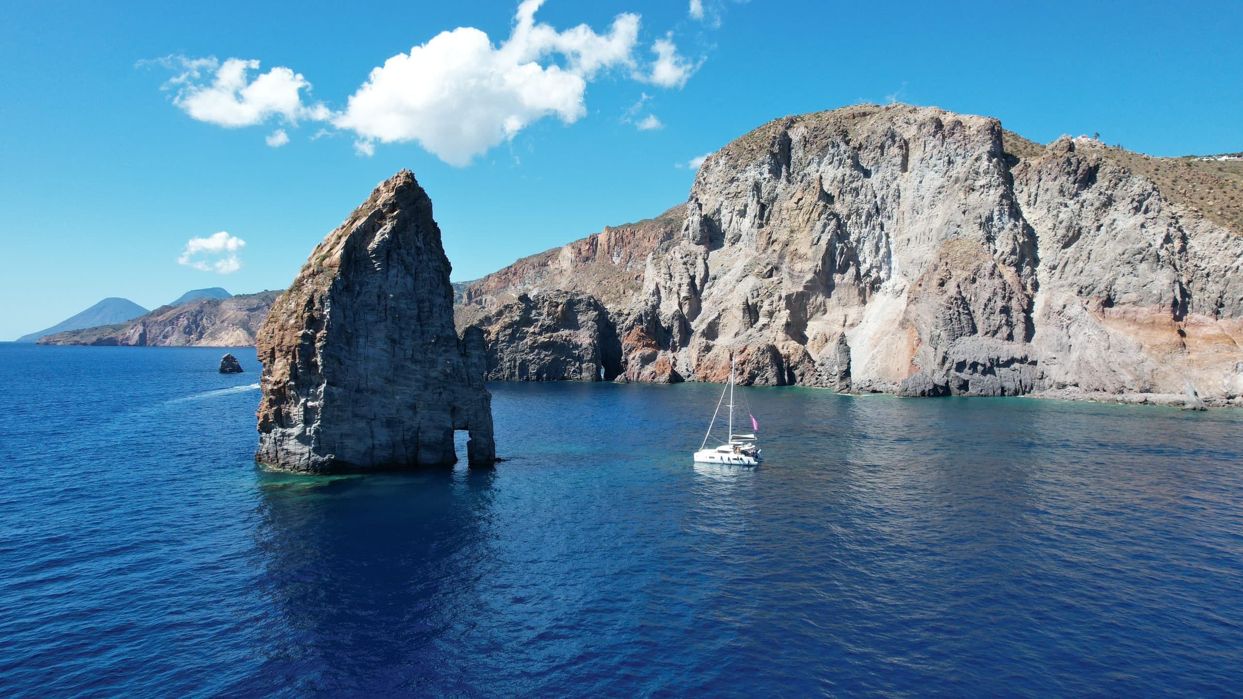 A catamaran at anchor beneath volcanic cliffs in the Aeolian Islands