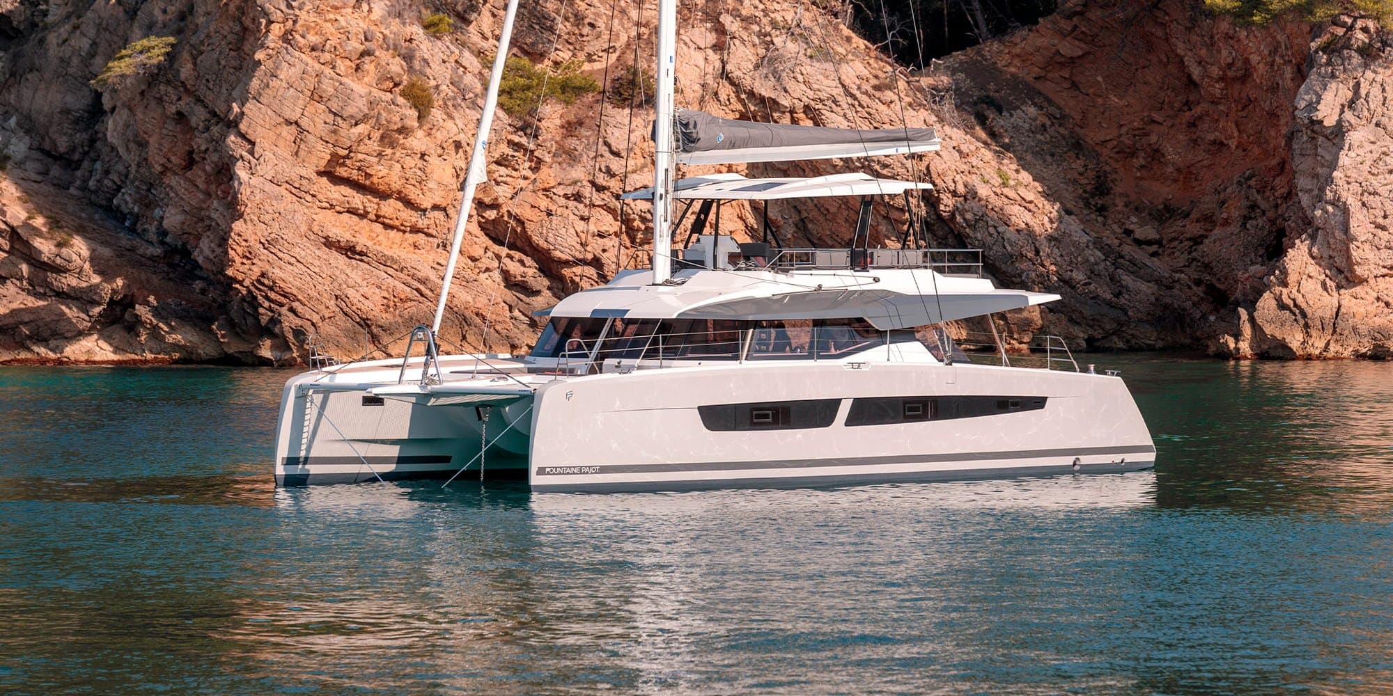 A Fountaine Pajot Thira 80 anchored beneath red cliffs
